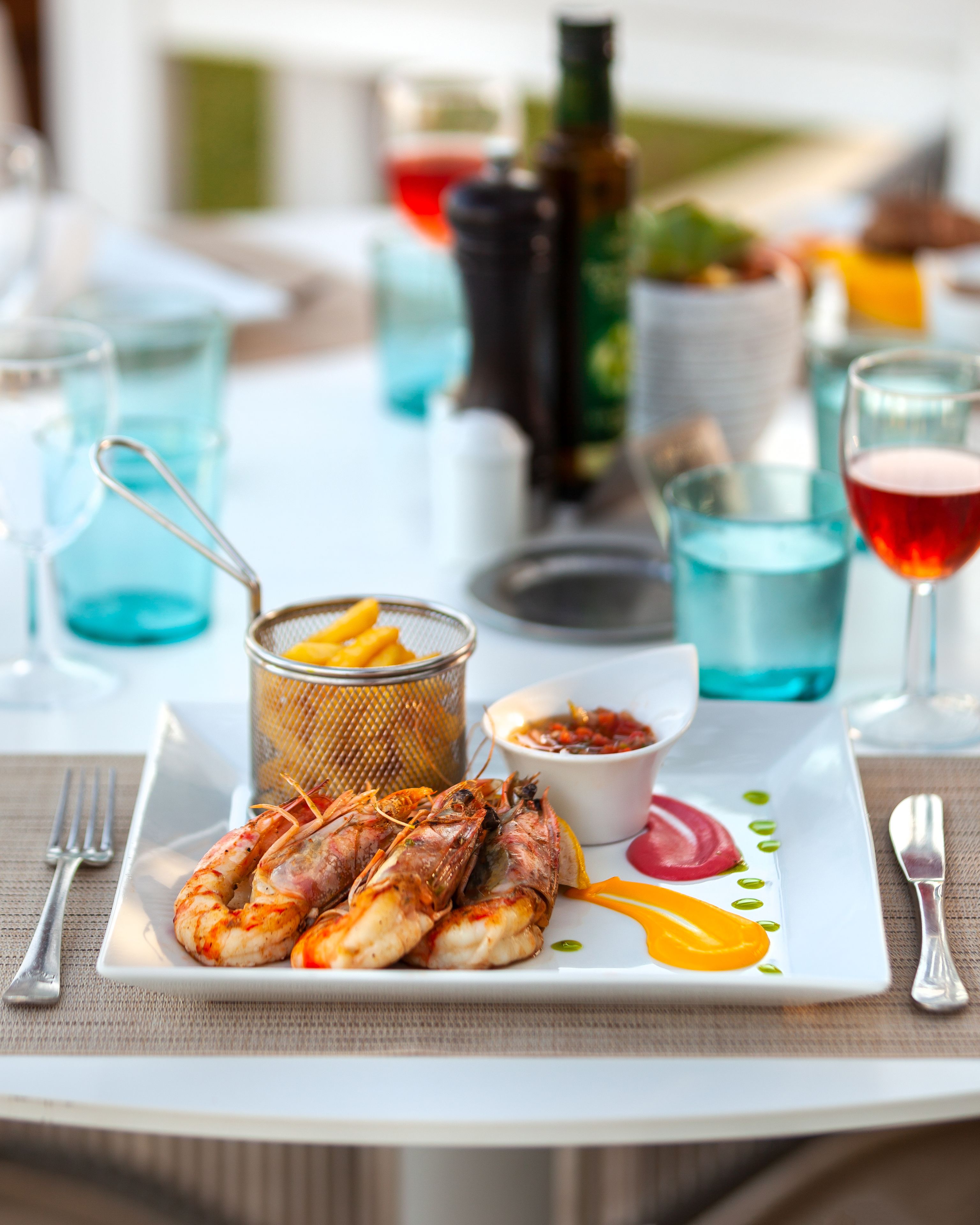 A seafood platter with grilled shrimp, a small bowl of sauce, and a glass of red wine on a table with a white placemat.