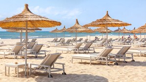 A beach with rows of sun loungers and thatched umbrellas.