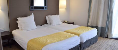 A hotel room with two beds, a nightstand, a mirror, a lamp, and a window with curtains.