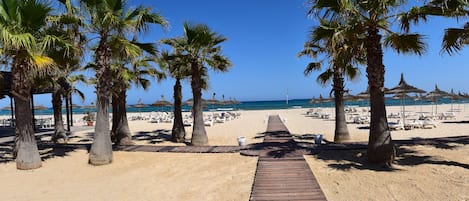 Een privéstrand, wit zand, ligstoelen aan het strand, parasols