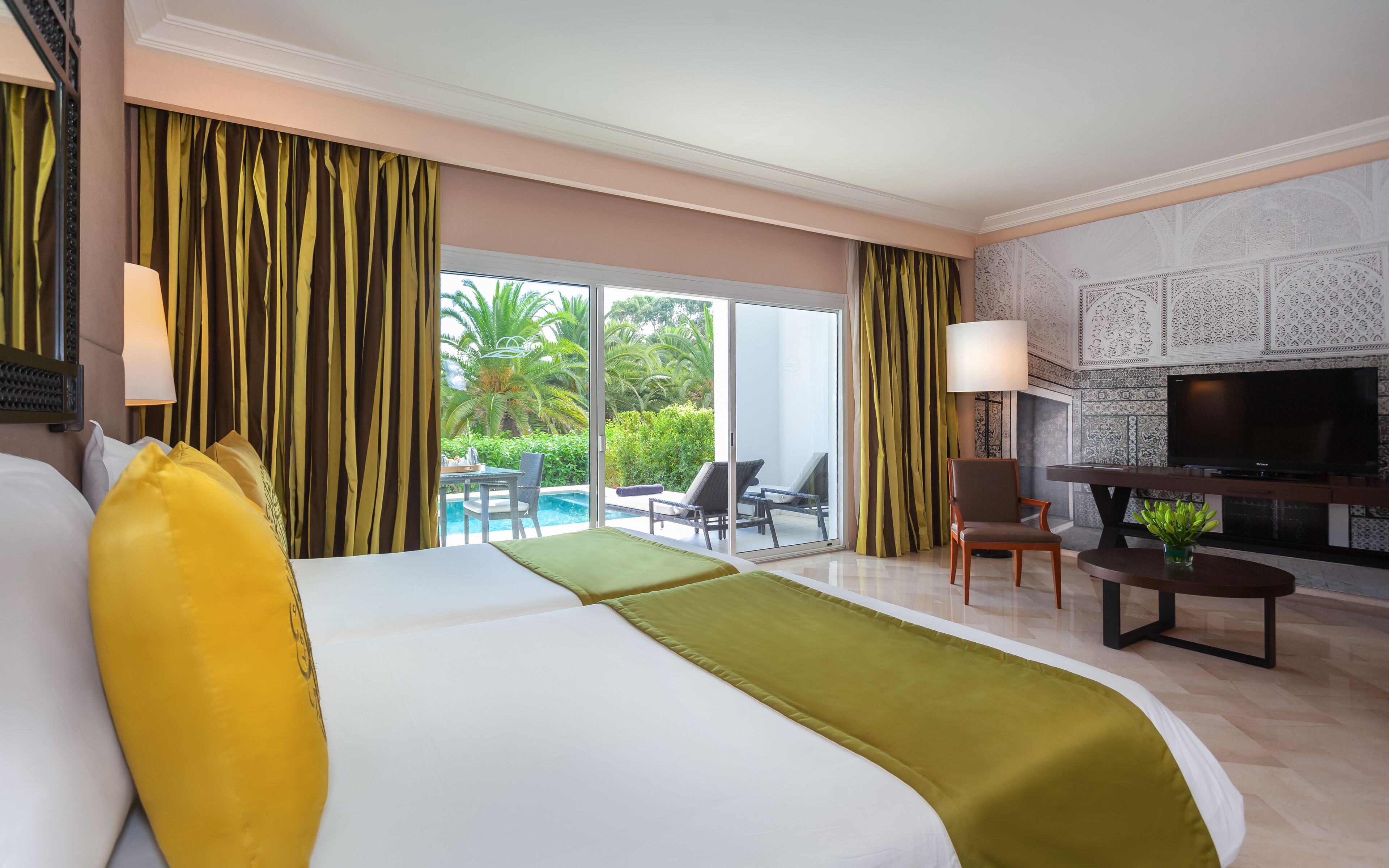 Hotelkamer met een groot bed, een televisie, een eettafel en uitzicht op een zwembad en groen.