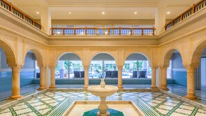 A spacious lobby with a central fountain, arched columns, and a balcony with a railing.