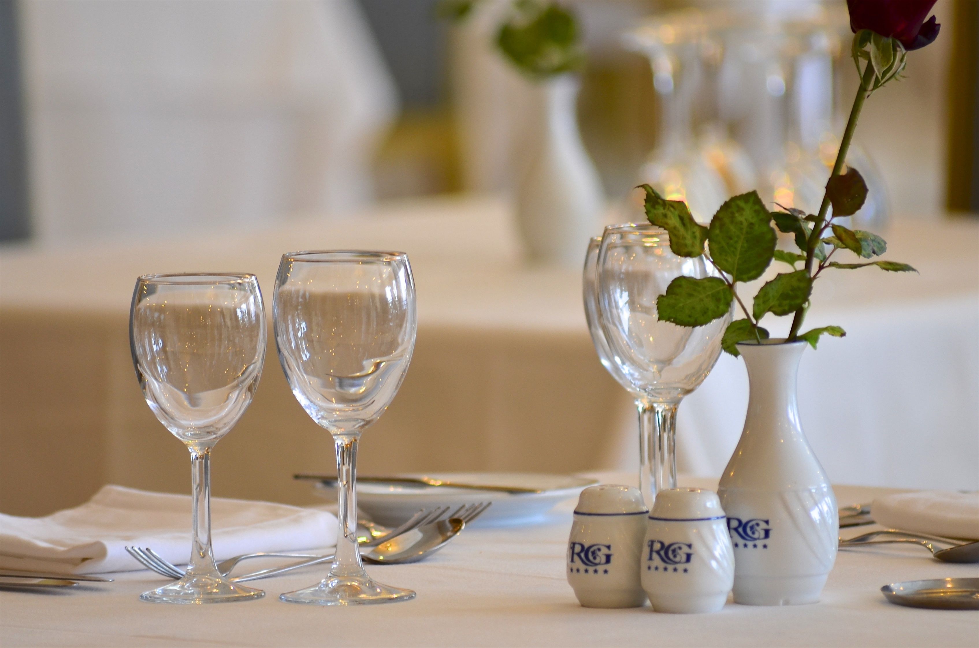 A table set with two wine glasses, a vase with a rose, and salt and pepper shakers.