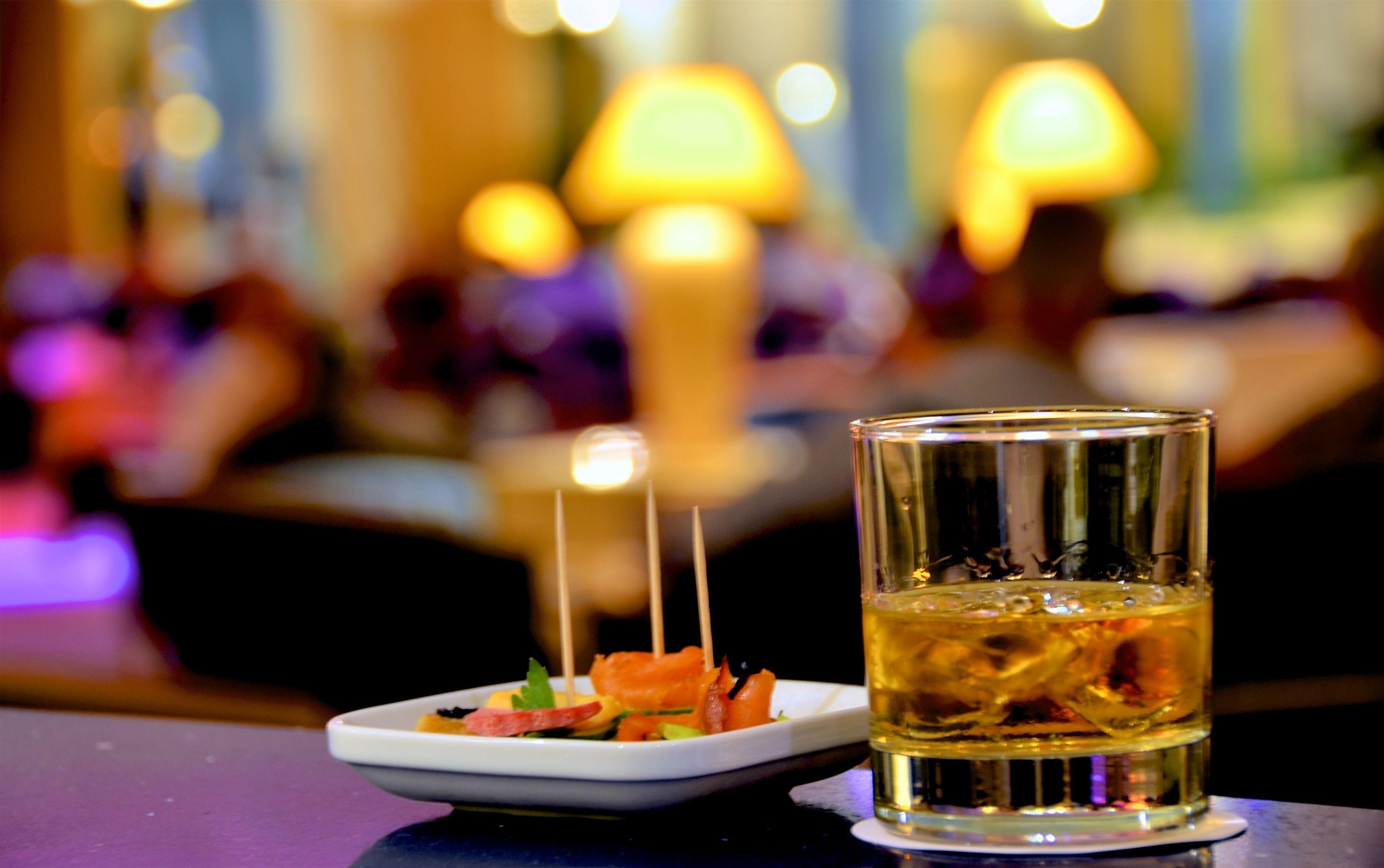 Un verre de whisky sur une table de bar, accompagné d’une petite assiette de nourriture.