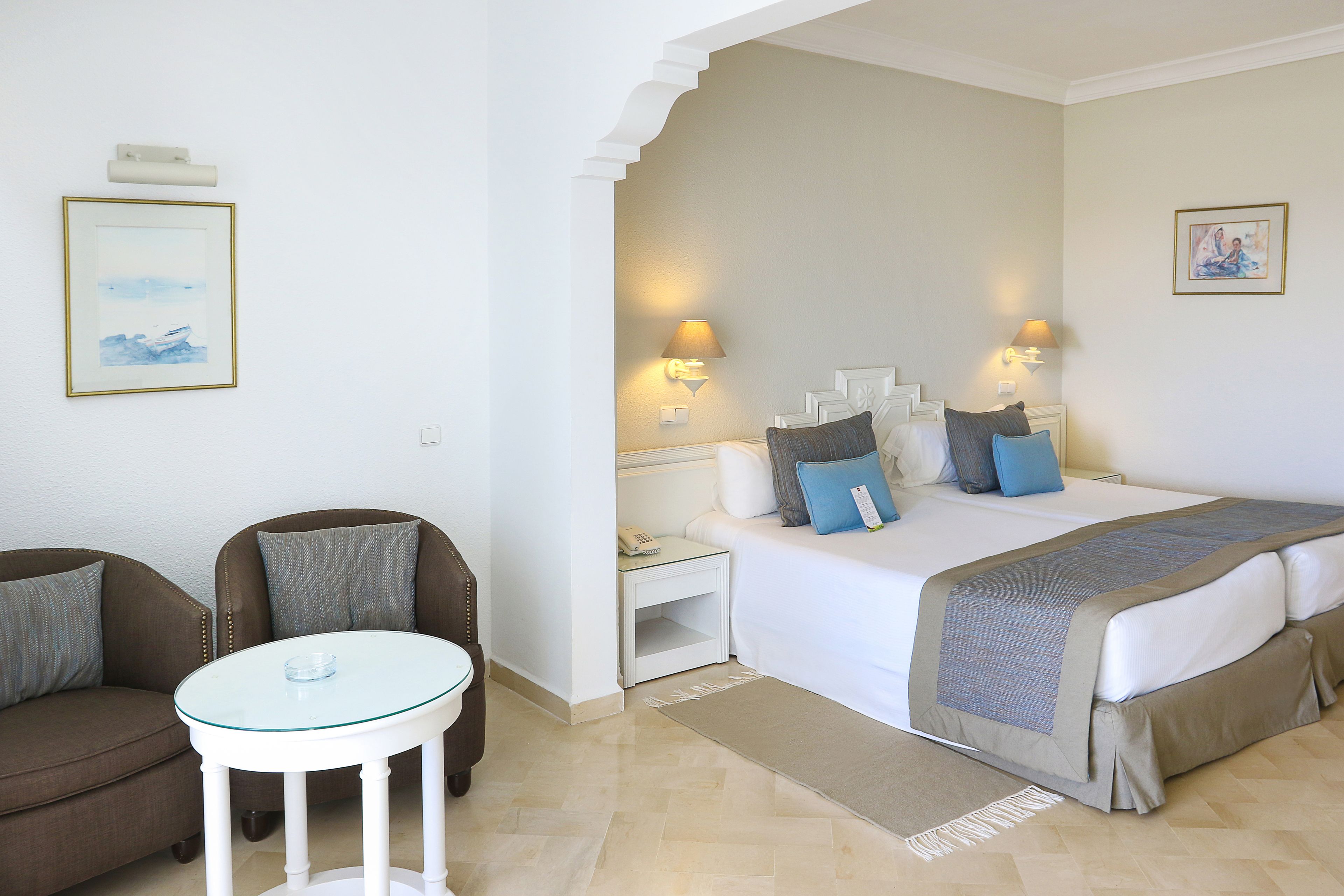 Une chambre d’hôtel comprenant un lit, deux tables de chevet, une petite table d’appoint, un canapé et une petite table ronde.