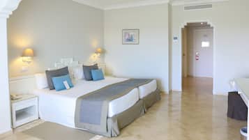Una habitación de hotel con una cama grande, lámparas de noche, una mesita de noche, una alfombra y una puerta que da a otra habitación.