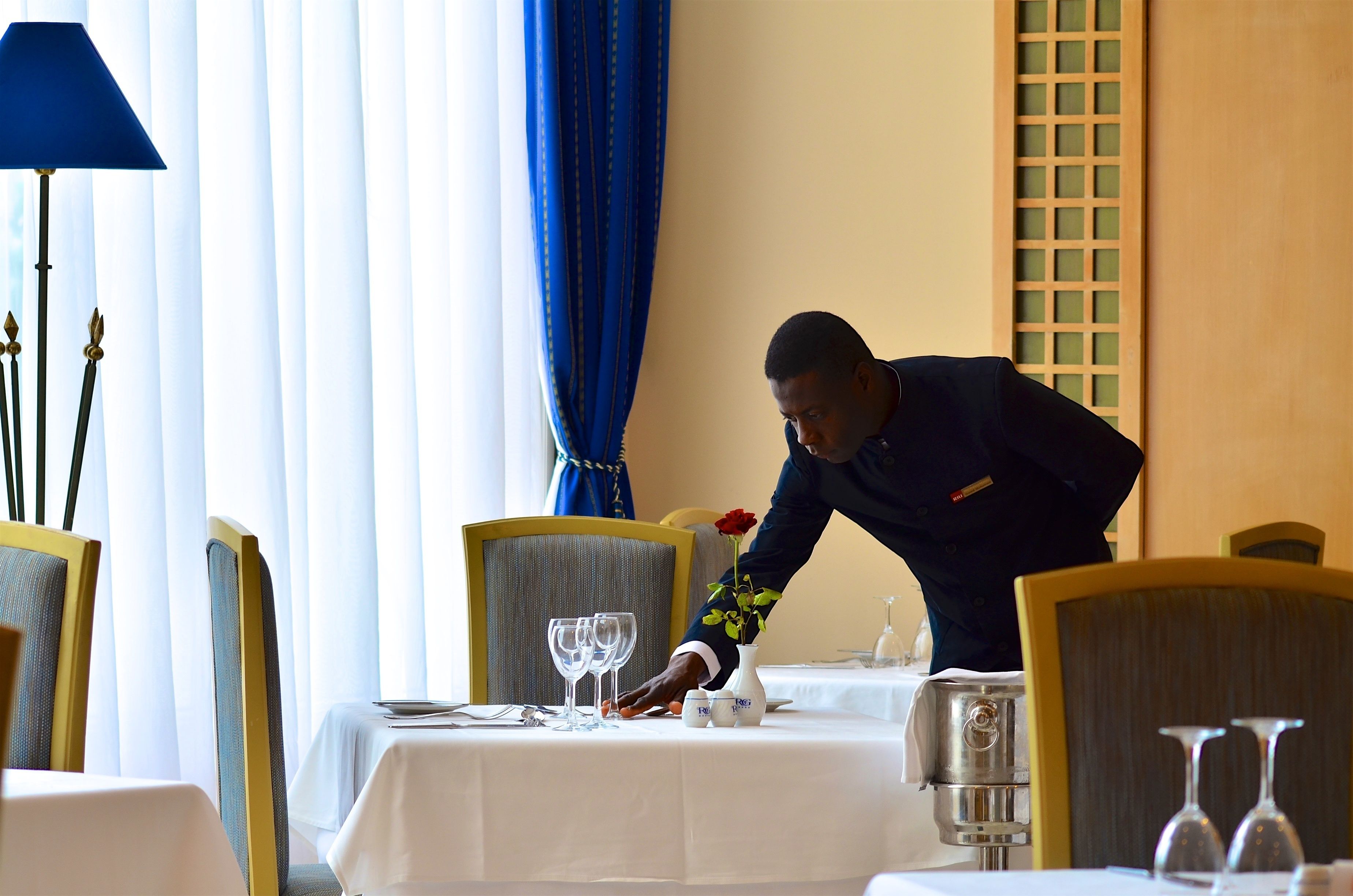 A well-set dining table with a waiter attending to it.