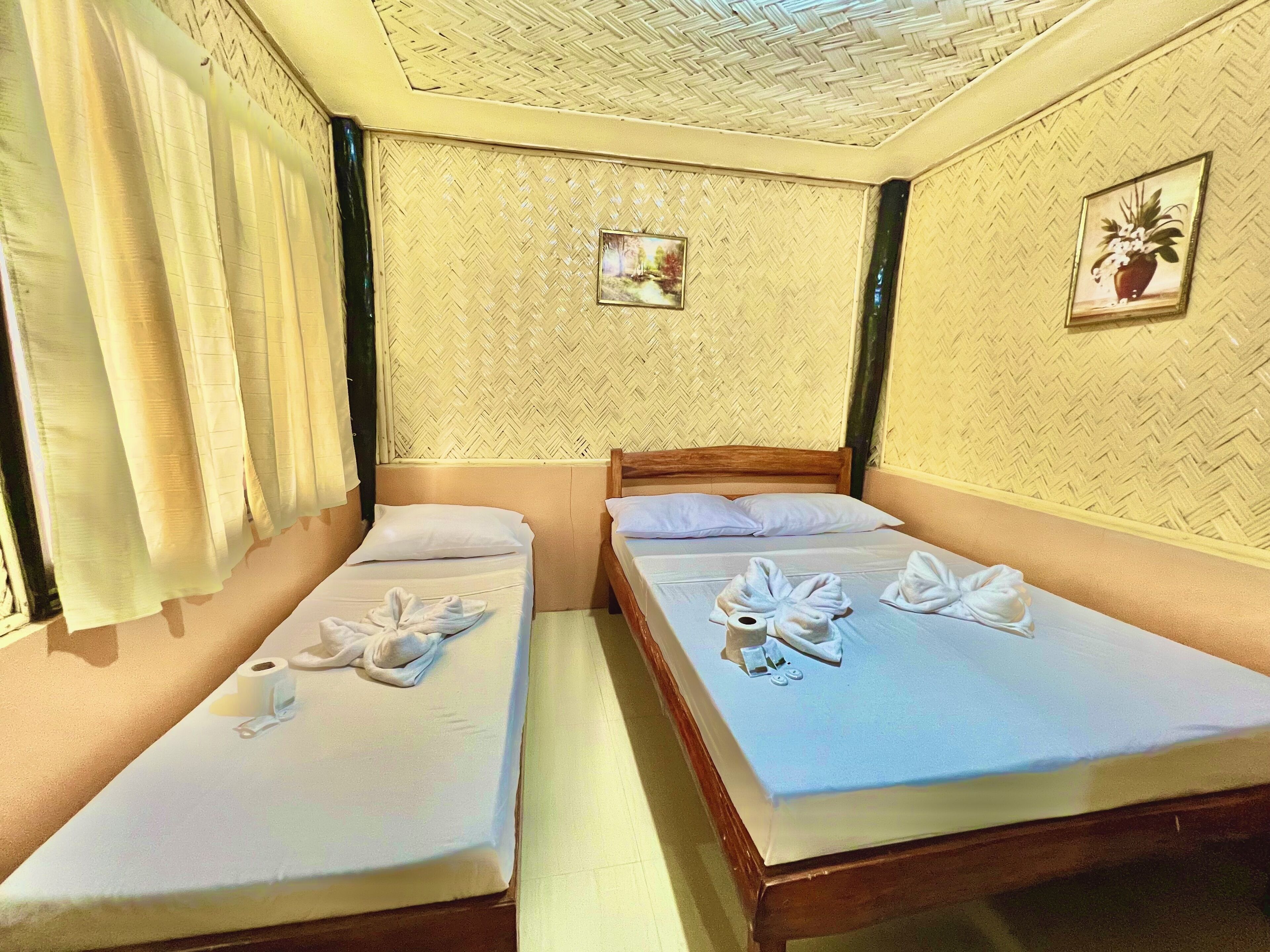 A hotel room with two single beds, each with neatly arranged towels and toiletries.