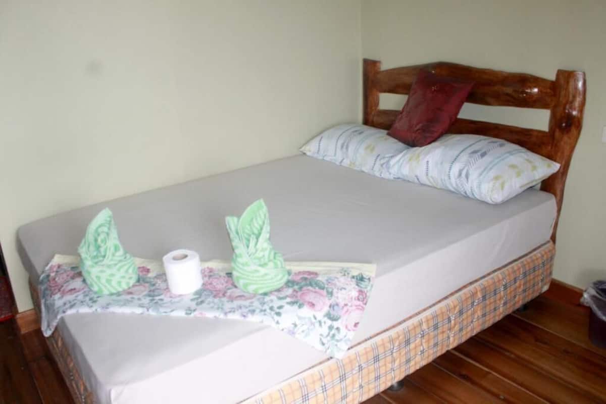A single bed with a wooden headboard, a floral bedspread, and two green decorative pillows.