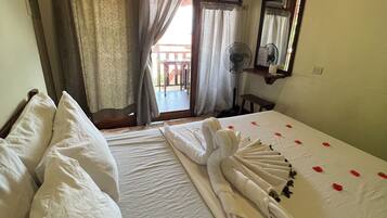 Habitación de hotel con dos camas, un ventilador y vistas al balcón exterior.