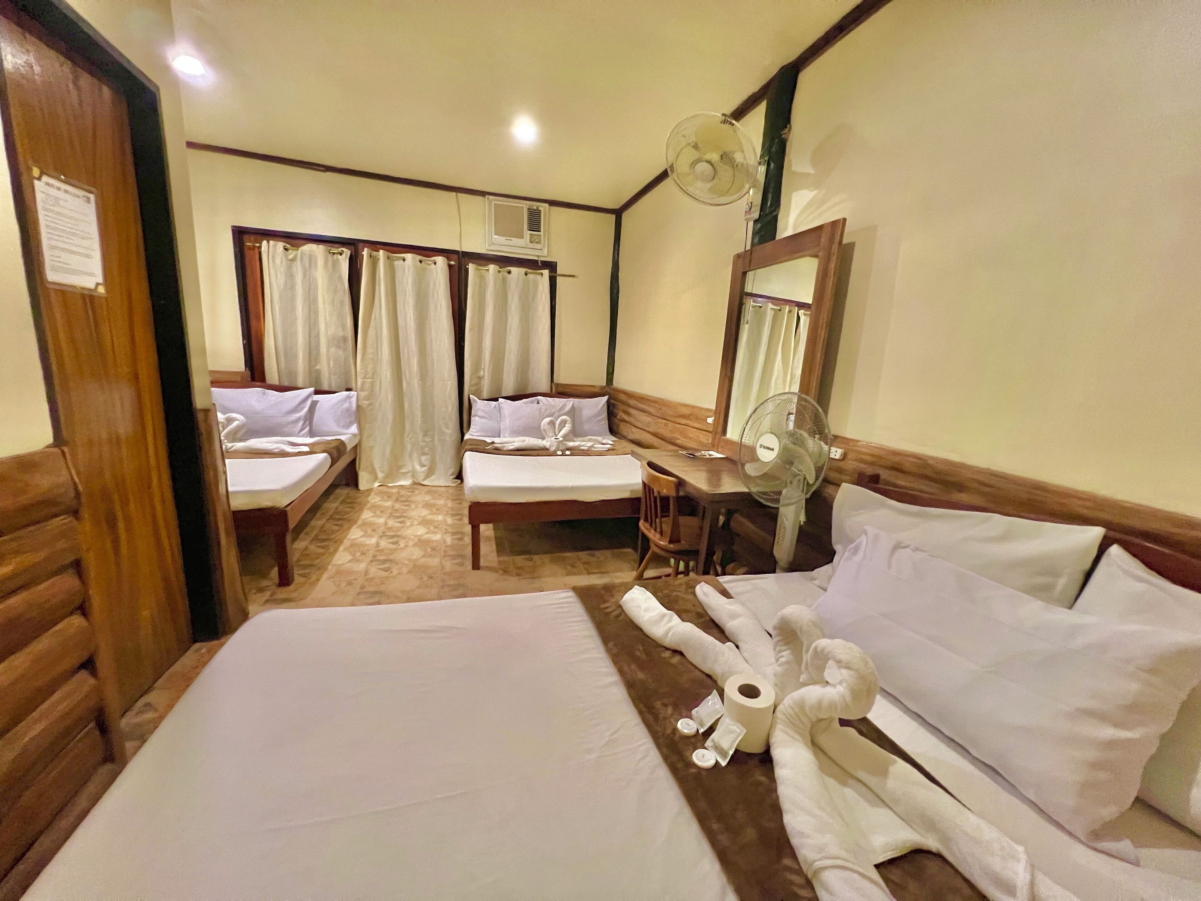 Habitación de hotel con dos camas, un escritorio, una silla, un ventilador y un espejo.