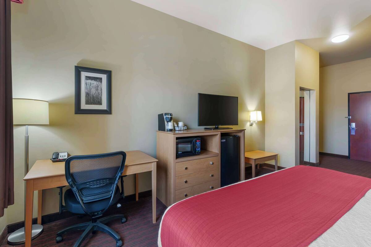 Ein Hotelzimmer mit Bett, Schreibtisch, Stuhl, Fernseher, Mikrowelle, Kühlschrank und einer Tür.
