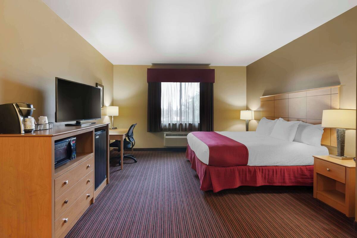 Ein Hotelzimmer mit Bett, Schreibtisch, Fernseher, Stuhl und Schreibtischlampe.