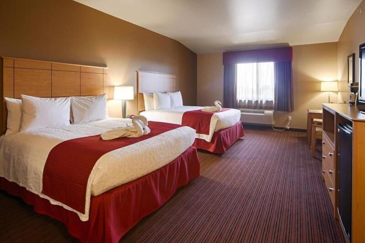 Ein Hotelzimmer mit zwei Betten, einem Schreibtisch, einem Schminktisch und einem Fenster mit Vorhängen.