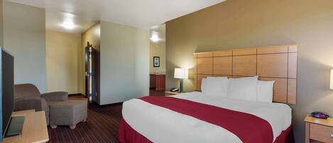 Une chambre d’hôtel avec un grand lit, un bureau, une chaise, une armoire et une table de chevet avec une lampe.