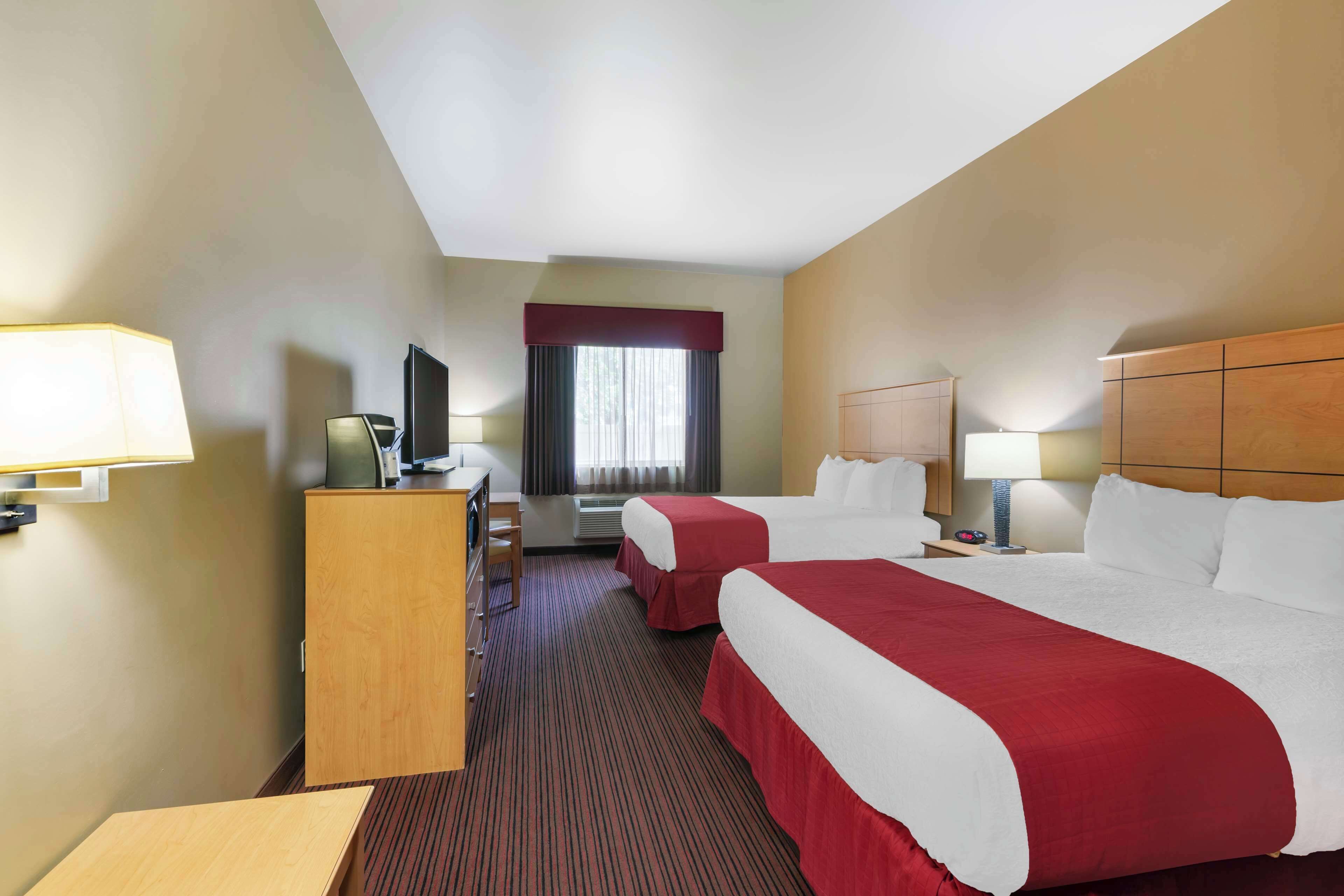 A hotel room with two beds, a desk, a television, and a window with curtains.
