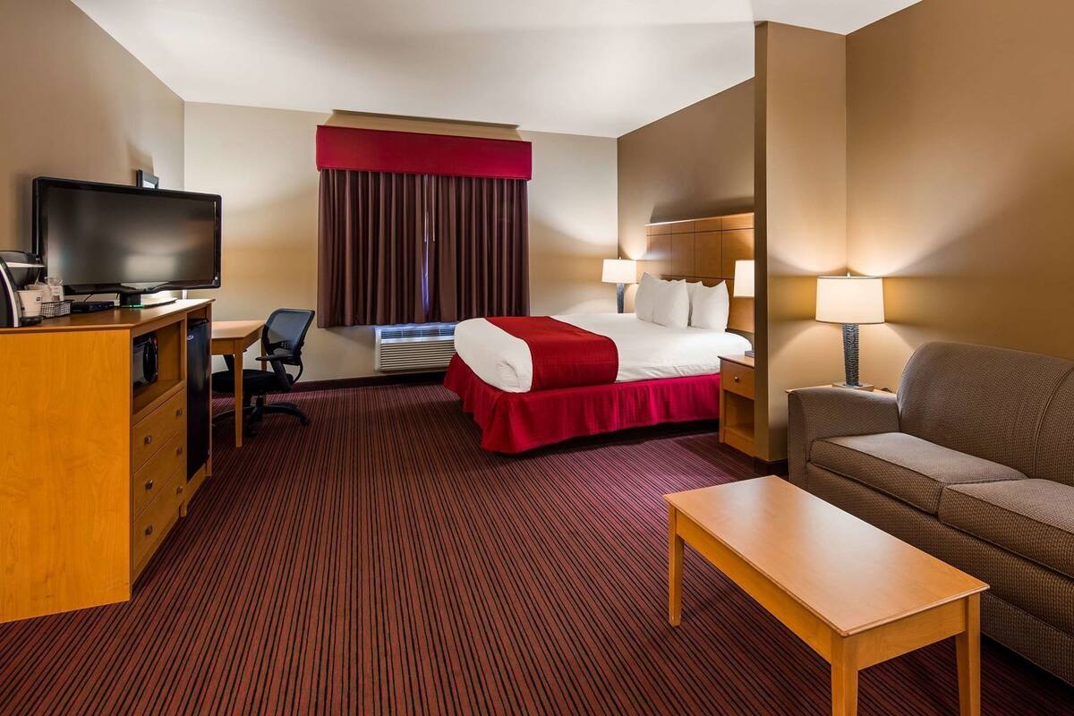 Ein Hotelzimmer mit einem Bett, einem Schreibtisch mit Fernseher, einer Couch und einer Lampe.