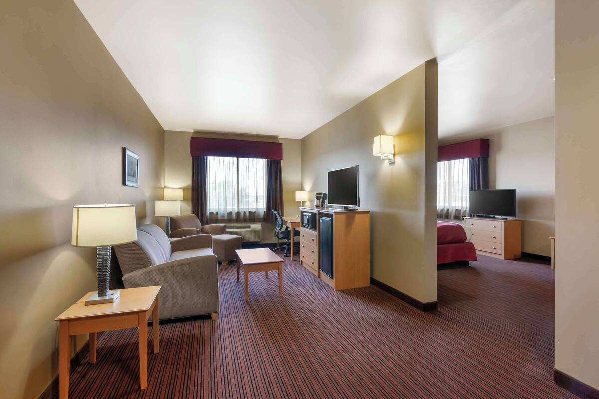 Ein Hotelzimmer mit Sofa, Sessel, Schreibtisch, Fernseher und einem kleinen Tisch.