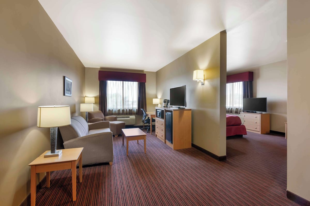 A hotel room with a sofa, armchair, desk, television, and a small table.