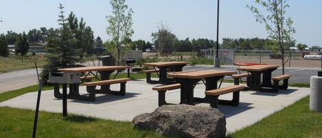 Un espace pique-nique équipé de plusieurs tables et bancs, entouré de pelouse et d’arbres.
