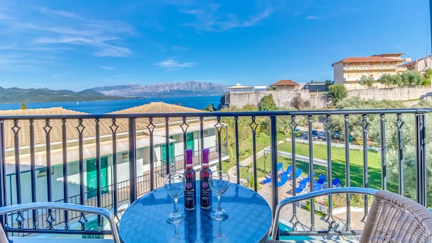A balcony with a table, two wine bottles, and glasses. A view of a building and mountains is visible in the background. - Vergina Star (Lefkada)