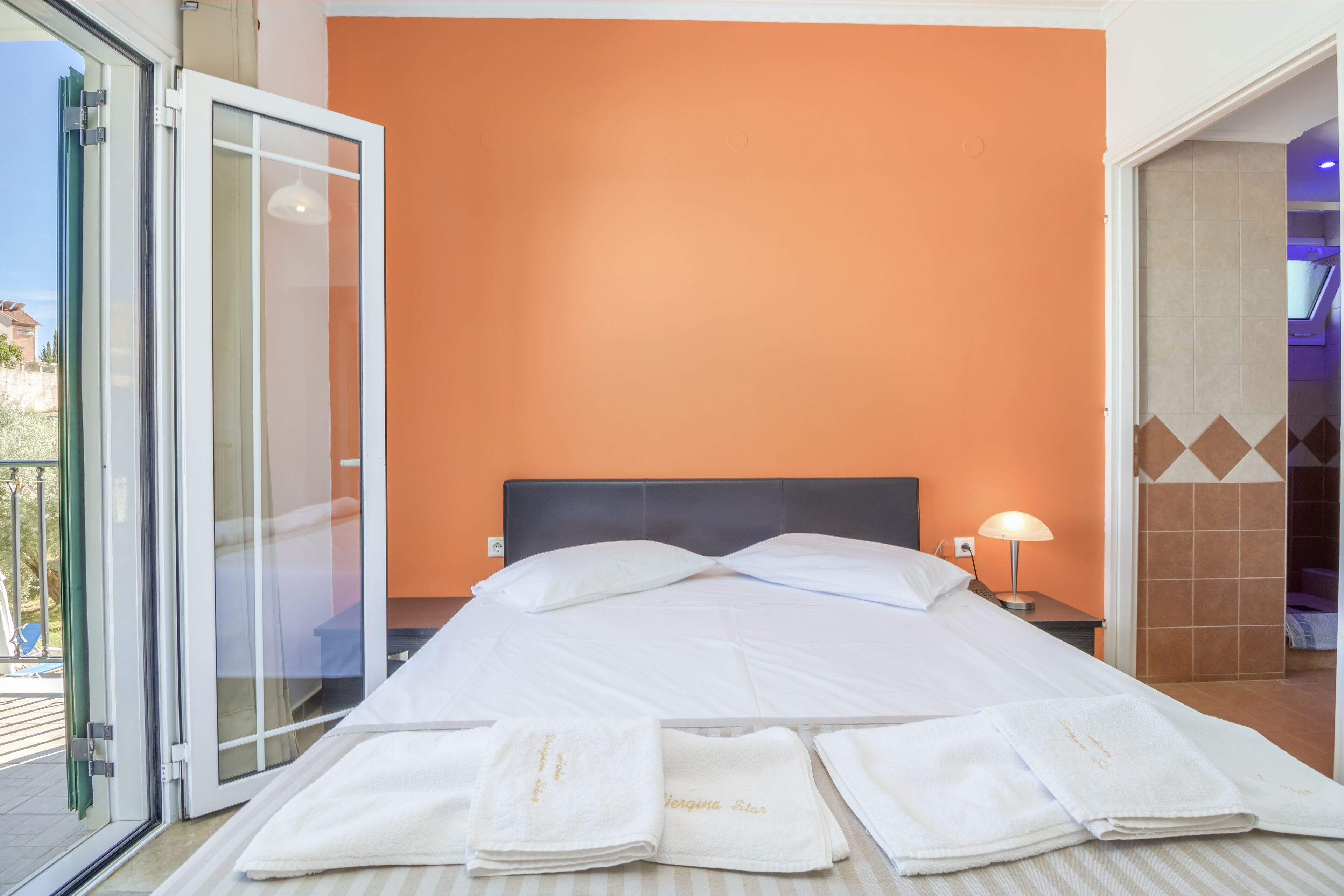 Une chambre d’hôtel comprenant un lit, une table de chevet, une lampe et une porte-fenêtre coulissante donnant sur un espace extérieur.