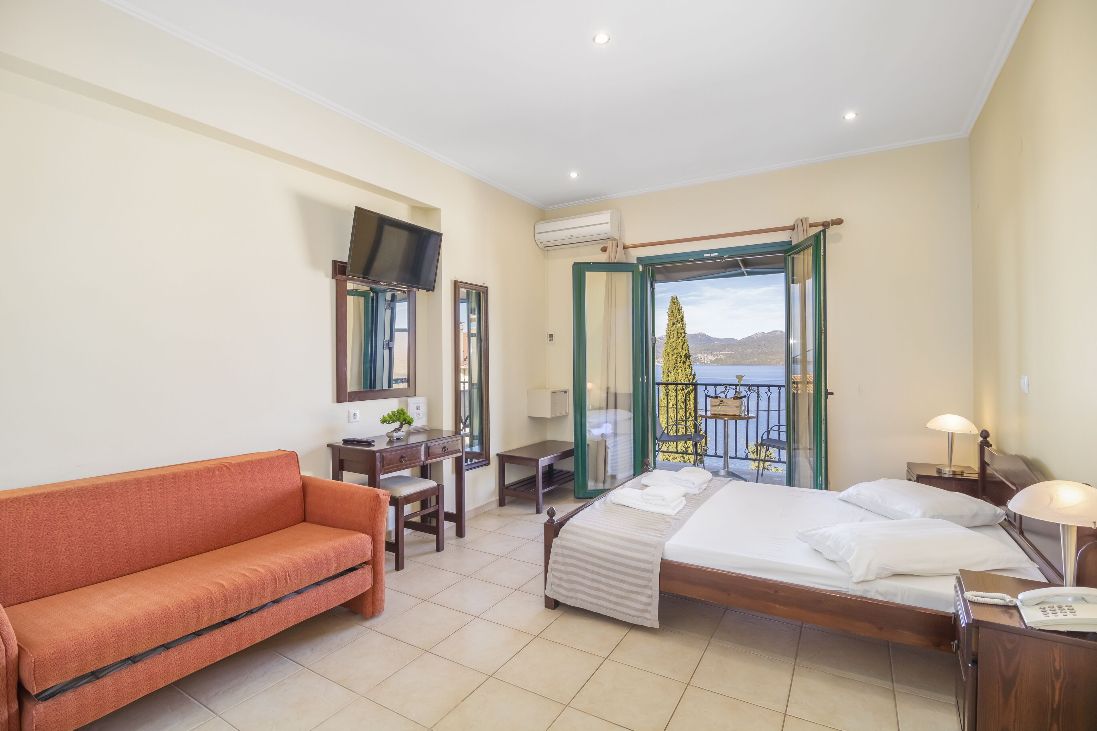 A hotel room with a bed, a sofa, a desk, a TV, and a balcony with a view.
