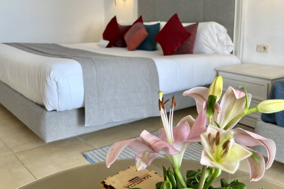 Ein ordentlich eingerichtetes Schlafzimmer mit einem Bett, Kissen, einer Nachttischlampe und einer Blumenkomposition auf einem Tisch.