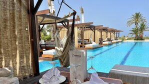 A dining table set with white napkins, plates, and cutlery, overlooking a pool with lounge chairs and palm trees. - hôtel Sentido Marillia Resort & Spa (Hammamet)
