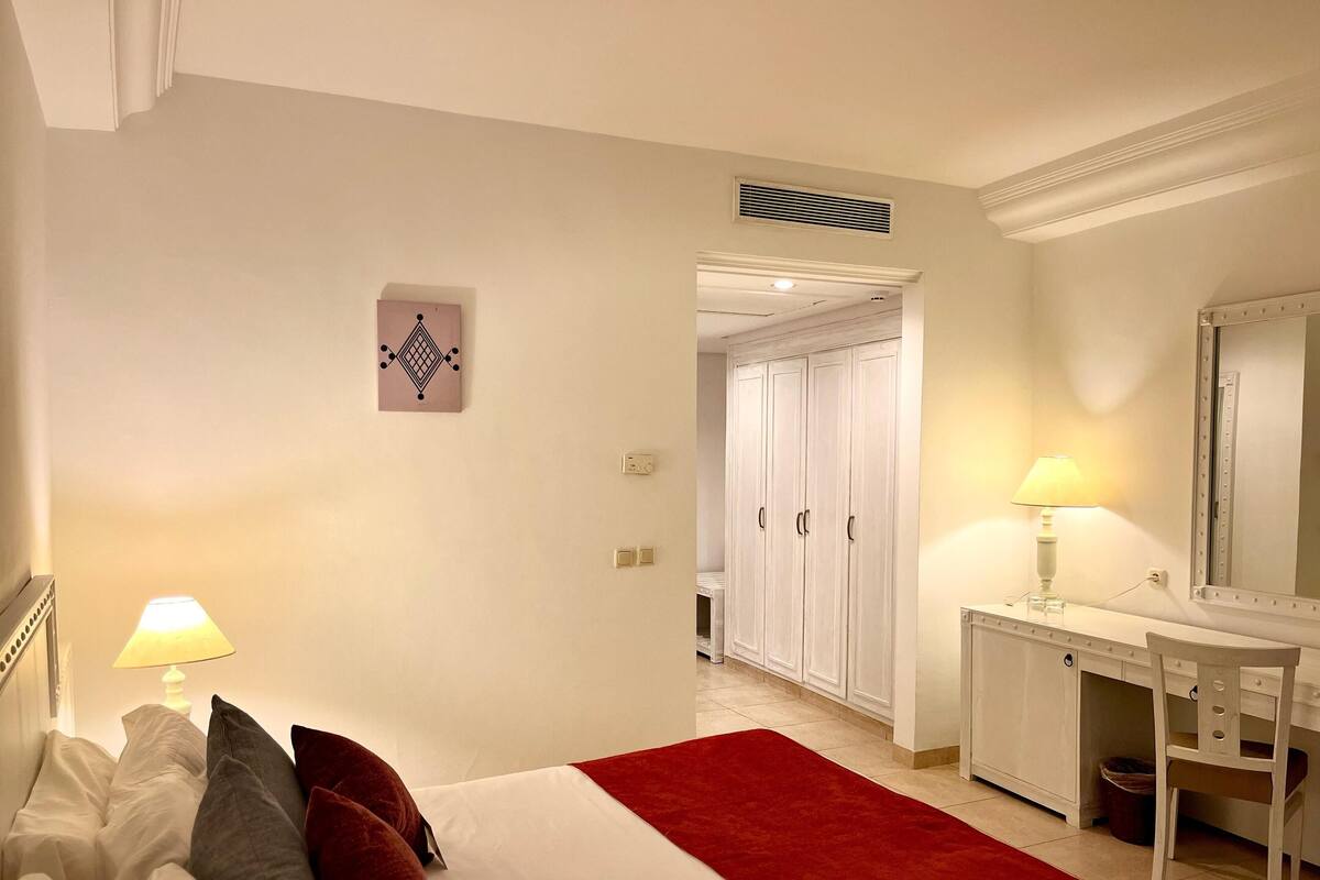 Ein Schlafzimmer mit einem Bett, Nachttischlampen, einem Schminktisch und einem roten Teppich.