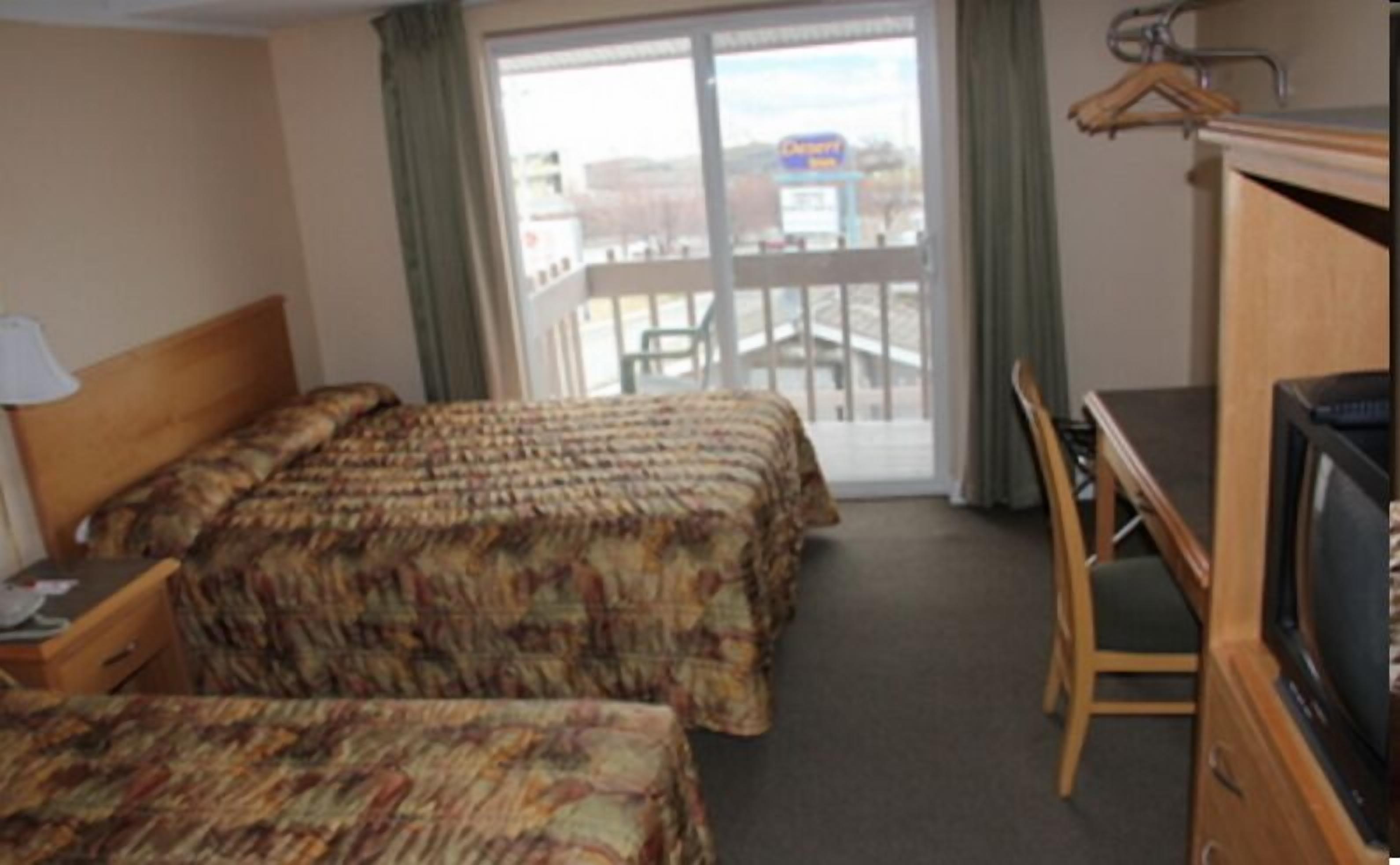 A hotel room with two beds, a desk, a chair, a TV, and a view of the outside.