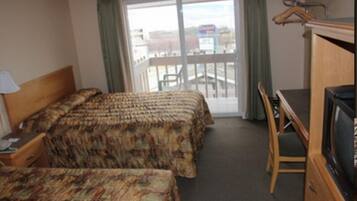 A hotel room with two beds, a desk, a chair, a TV, and a view of the outside.