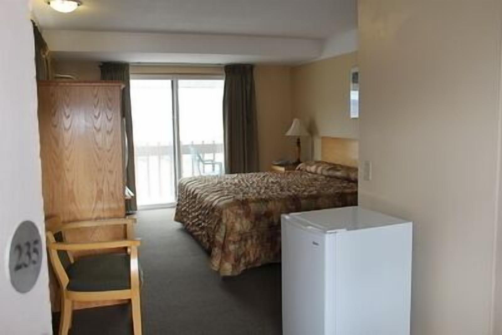 Habitación de hotel con cama, escritorio, silla, refrigerador y vista al exterior.