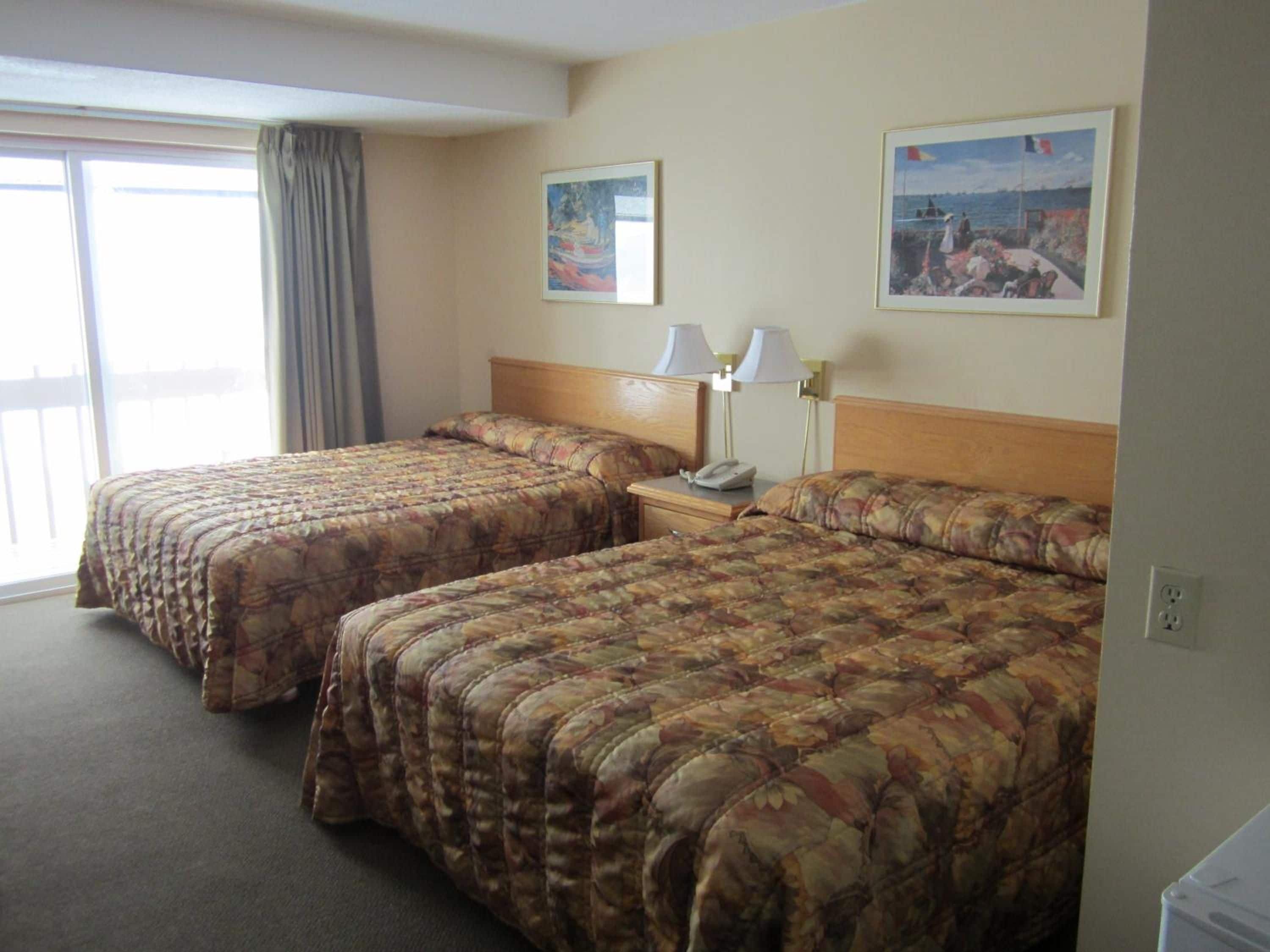A hotel room with two beds, a nightstand with a lamp, and a window with curtains.