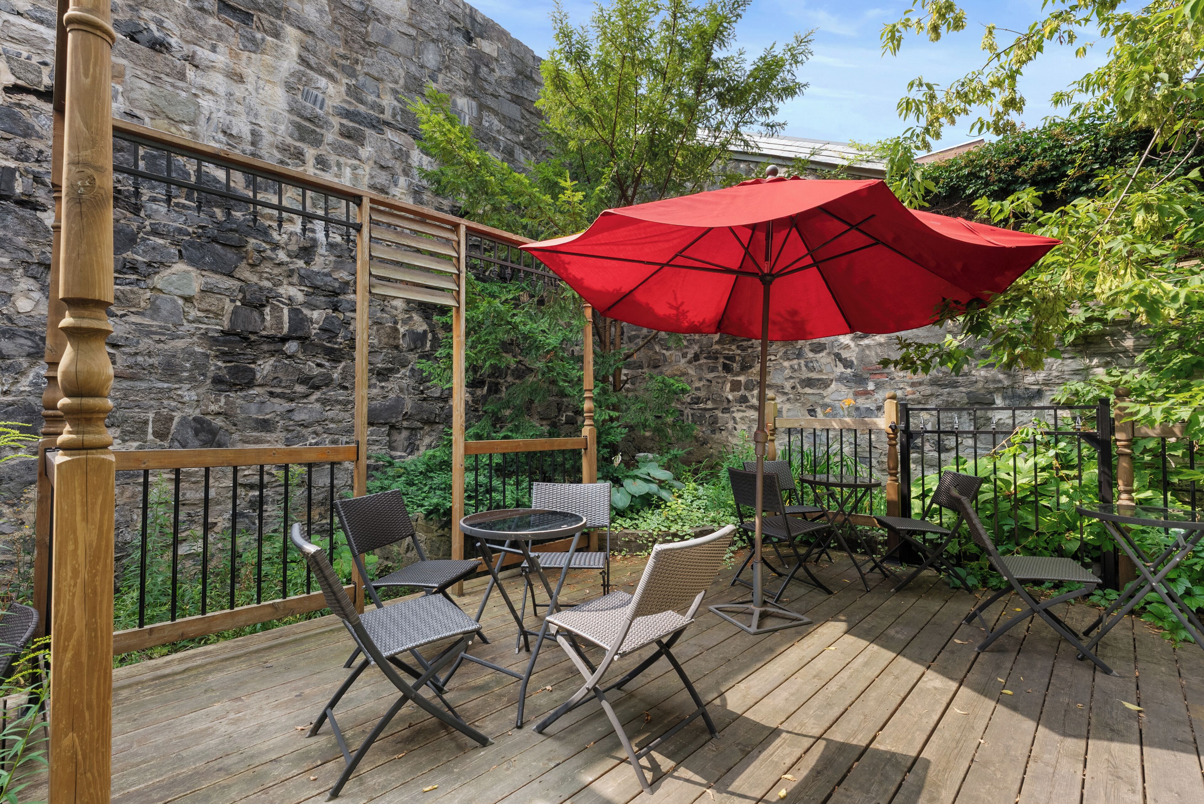 Una terraza de madera con mobiliario exterior y un paraguas rojo.