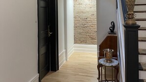A hallway with a black door, a staircase with a light fixture, and a brick wall in the background. - Hotel Le Château de Pierre (Québec City)