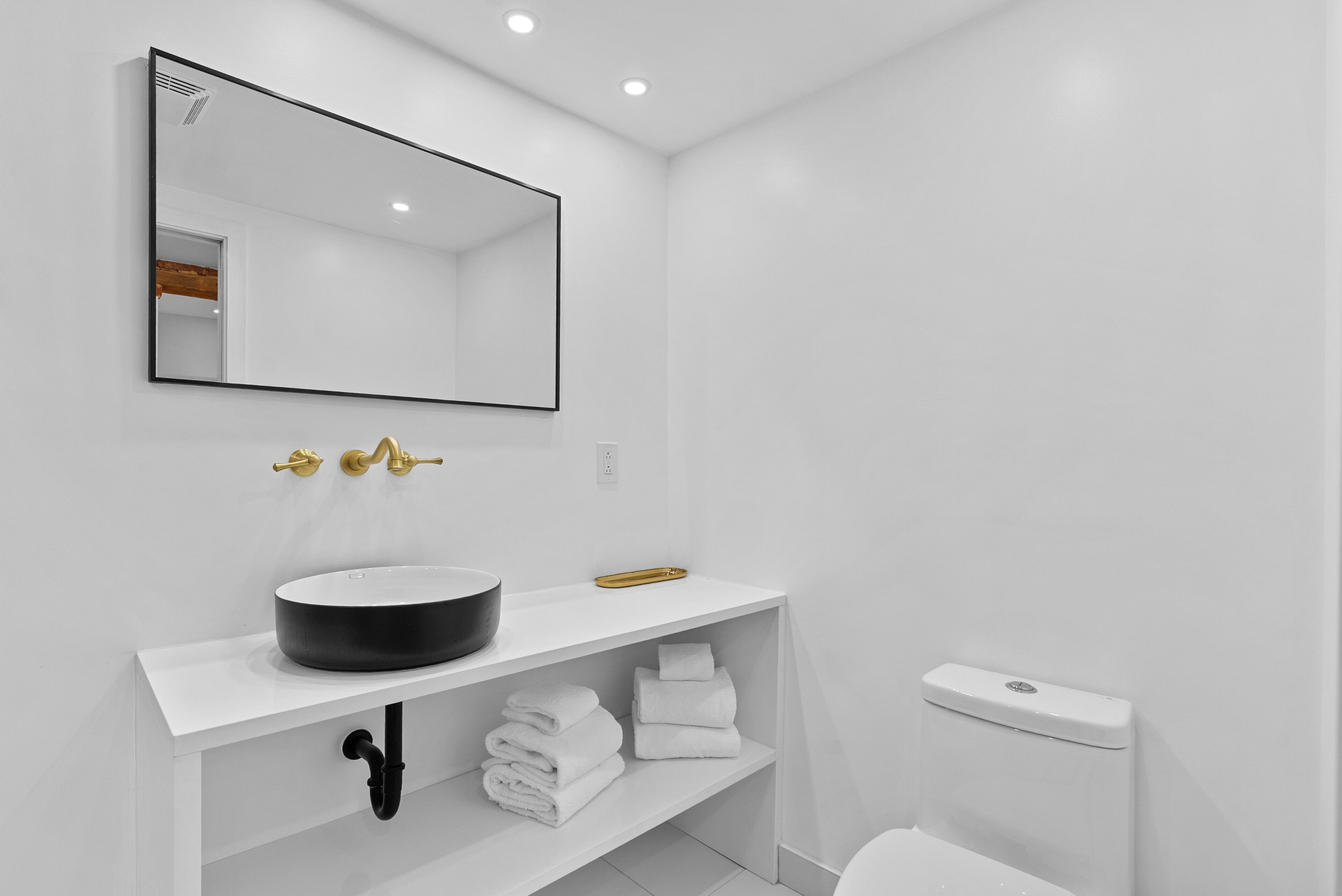 A modern bathroom with a white sink, a large mirror, and a toilet.