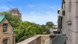 A balcony with a stone balustrade, a metal chair, and a view of a historic building with a steep roof. - Hotel Le Château de Pierre (Québec City)