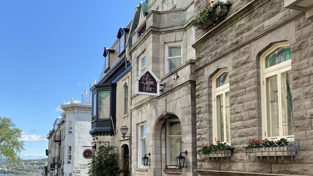 A row of historic stone buildings with balconies, a sign for 'Chateau Pierre', and a view of a body of water. - Hotel Le Château de Pierre (Québec City)