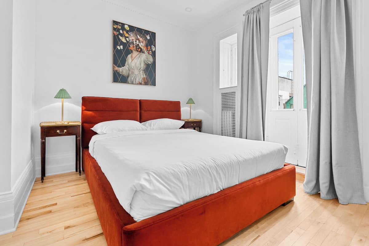 Quarto com cama grande, duas mesas de cabeceira, um quadro na parede e uma janela com cortinas.