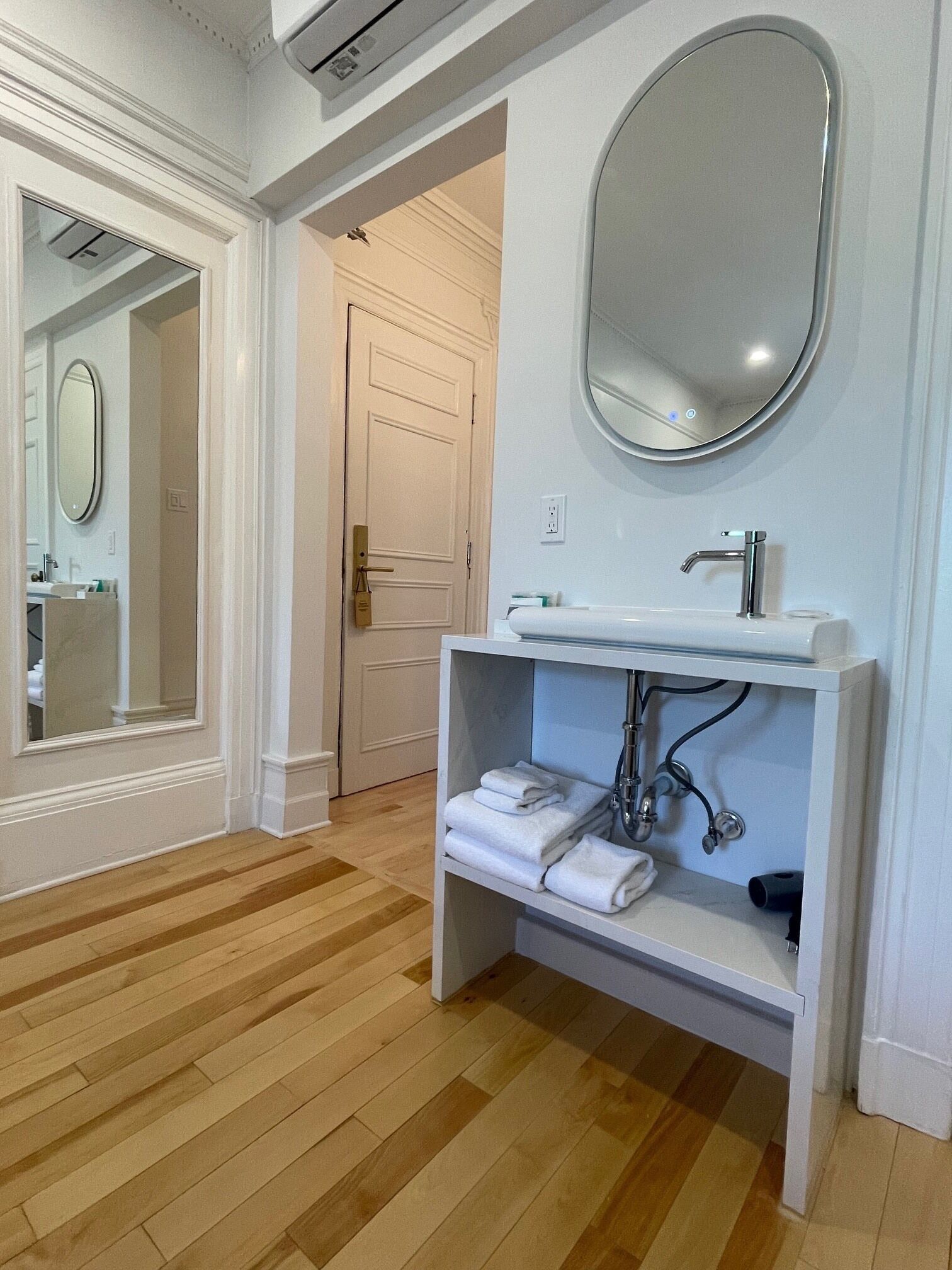 Un baño con lavamanos blanco, espejo y toallero.