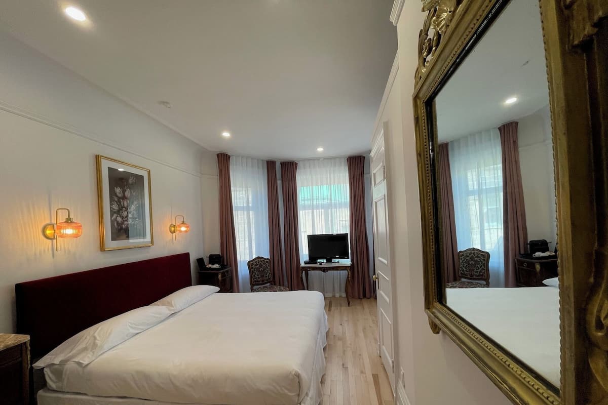 Quarto de hotel com uma cama grande, uma escrivaninha com computador, televisão e um espelho amplo.