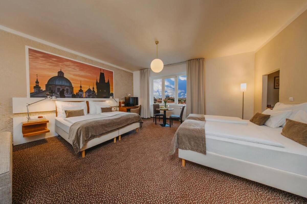 Hotelkamer met twee bedden, een bureau, een stoel, een lamp en een groot schilderij van een stadsgezicht.