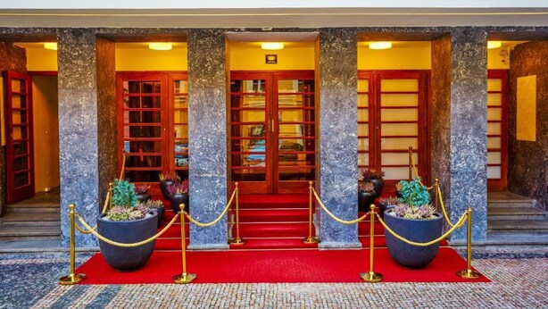 L’entrée d’un hôtel, avec ses colonnes de marbre, son tapis rouge et ses plantes en pot.