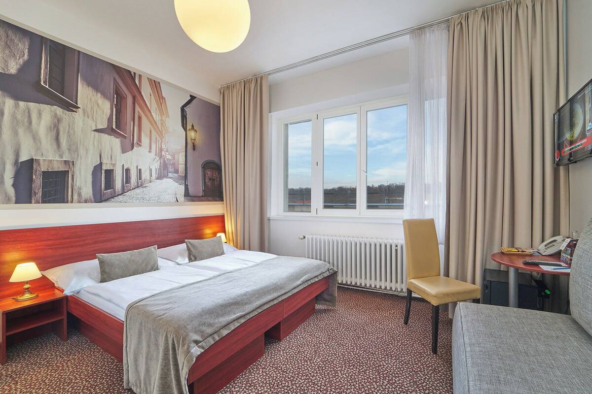 Een hotelkamer met een groot bed, een stoel, een bureau met telefoon en een raam met gordijnen.