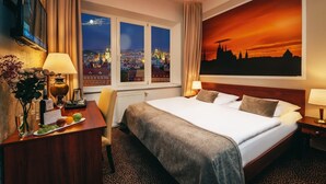 Une chambre d’hôtel avec un grand lit, un bureau avec une lampe, une télévision et une vue sur la ville par la fenêtre.