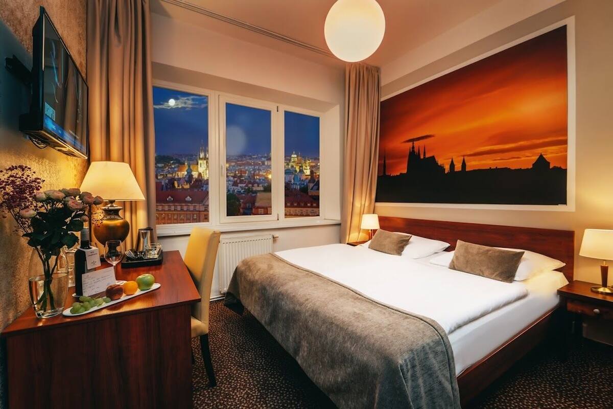 Hotelkamer met een groot bed, een bureau met lamp, een televisie en uitzicht op de stad.