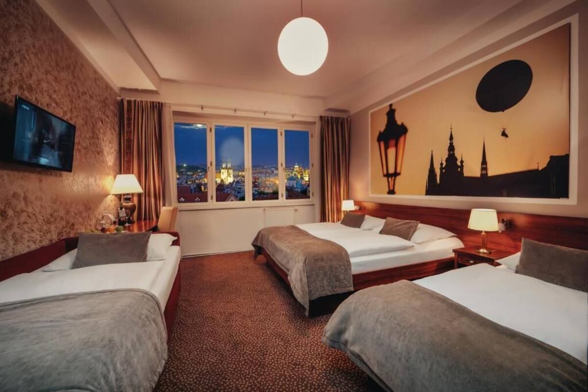 Een hotelkamer met twee bedden, een groot raam met uitzicht over de stad, een tv aan de muur en een schilderij van een stadsgezicht.