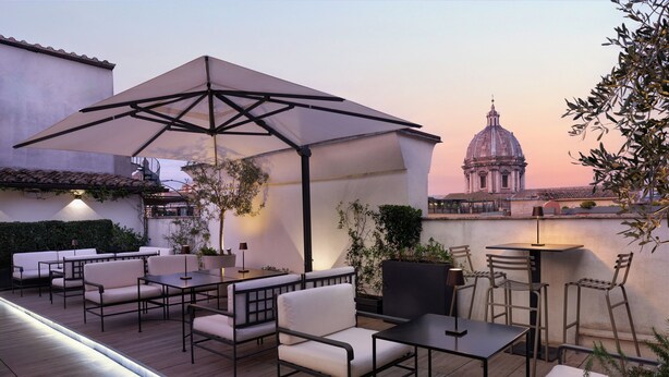Un patio exterior con asientos y un paraguas grande, con vistas a un edificio histórico.