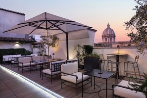 Un patio exterior con asientos y un paraguas grande, con vistas a un edificio histórico.